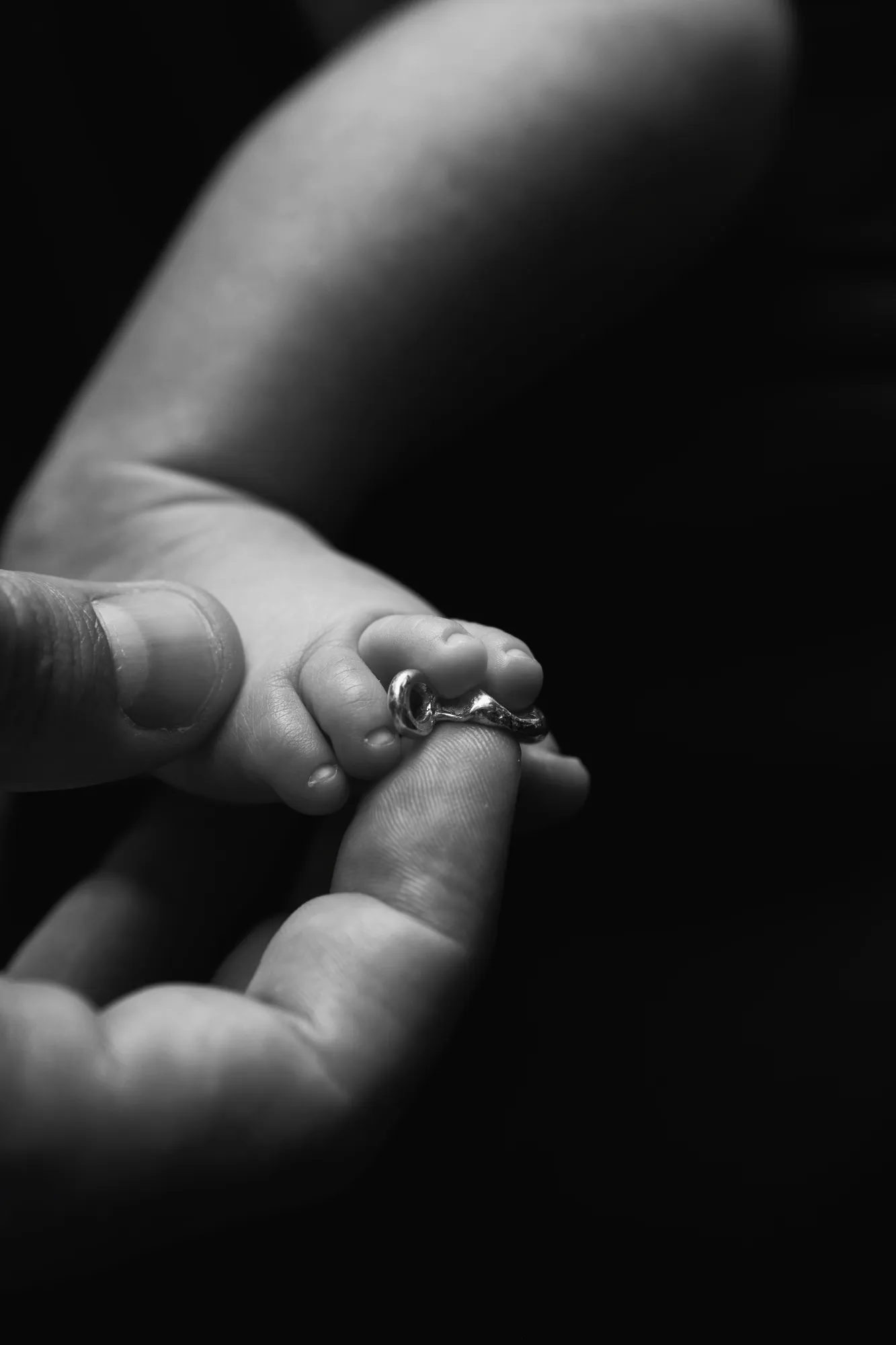 Una mano adulta sostiene el pie de un bebé, con una pieza de joyería sobre los dedos.