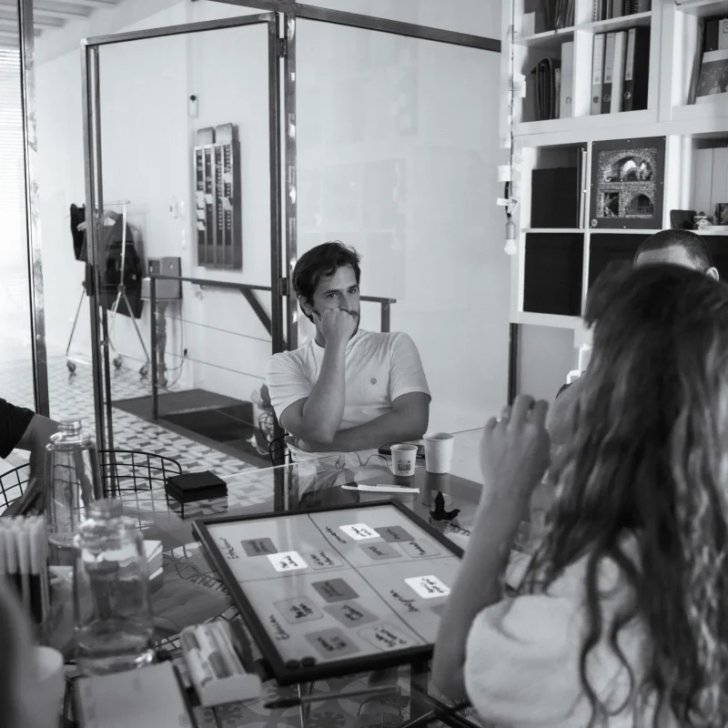 Una persona escuchando durante una reunión; en primer término, un panel con muestras impresas sobre la mesa.